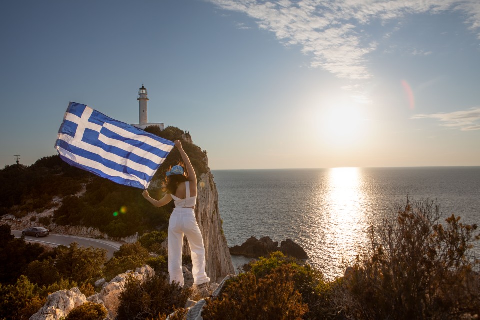 Femme brandissant un drapeau grec à Lefkada au coucher du soleil en Grece en mars